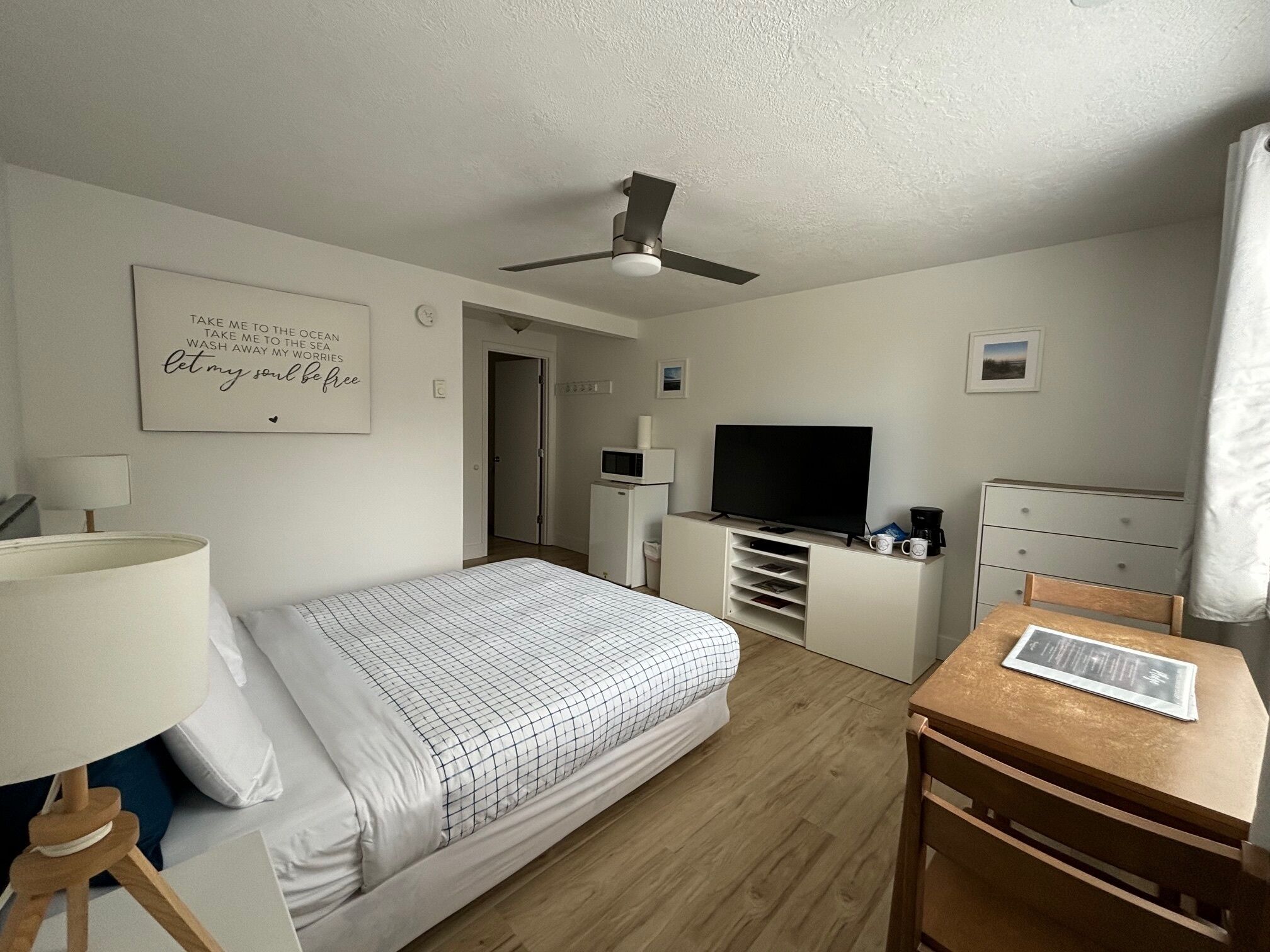 Una habitación de hotel con cama, escritorio, televisor, ventilador de techo y una pared con una cita motivacional.