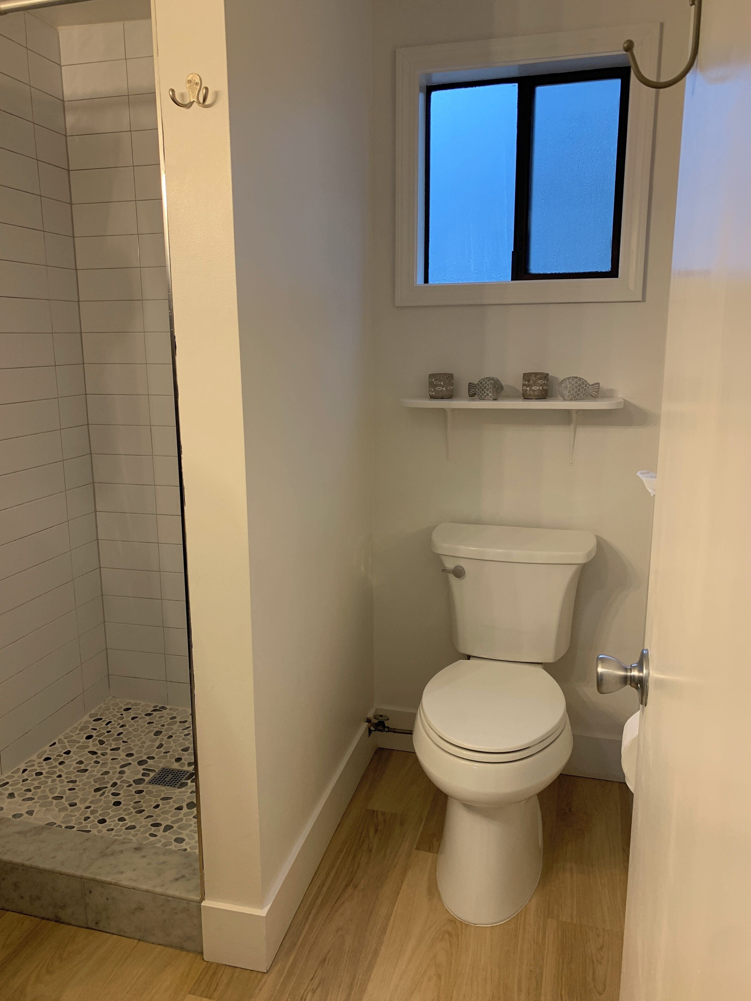 A bathroom with a shower, toilet, and a window above the sink.