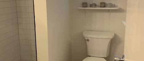 A bathroom with a shower, toilet, and a window above the sink.