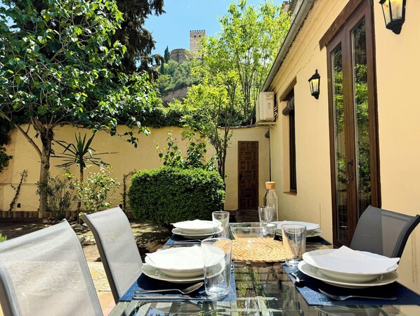 An outdoor dining area with a table set for four, surrounded by greenery and a view of a castle in the distance.