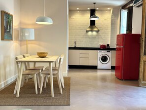 A modern kitchen with a built-in washing machine, a dining area with a table and chairs, and pendant lighting.
