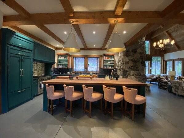 A spacious kitchen with a large island, bar stools, and wooden beams.