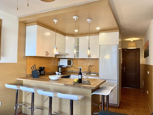 A modern kitchen with wooden cabinets, a central island with bar stools, a microwave, and a refrigerator.