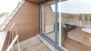 Une terrasse moderne sur le toit, dotée d’une plateforme en bois, d’une porte vitrée donnant sur un espace de détente extérieur et offrant une vue dégagée sur le paysage environnant.