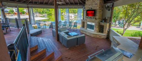 A covered outdoor patio with a stone fireplace, seating area, and a television screen displaying ESPN.