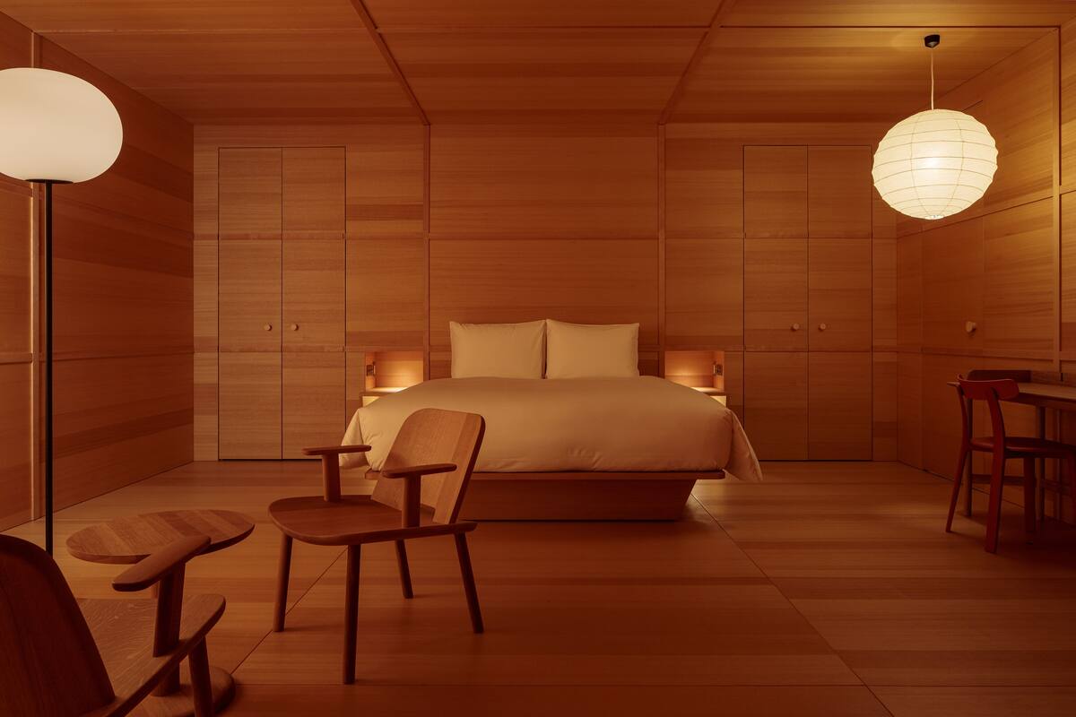 A modern bedroom with a large bed, wooden flooring, and a dining area with a table and chairs.