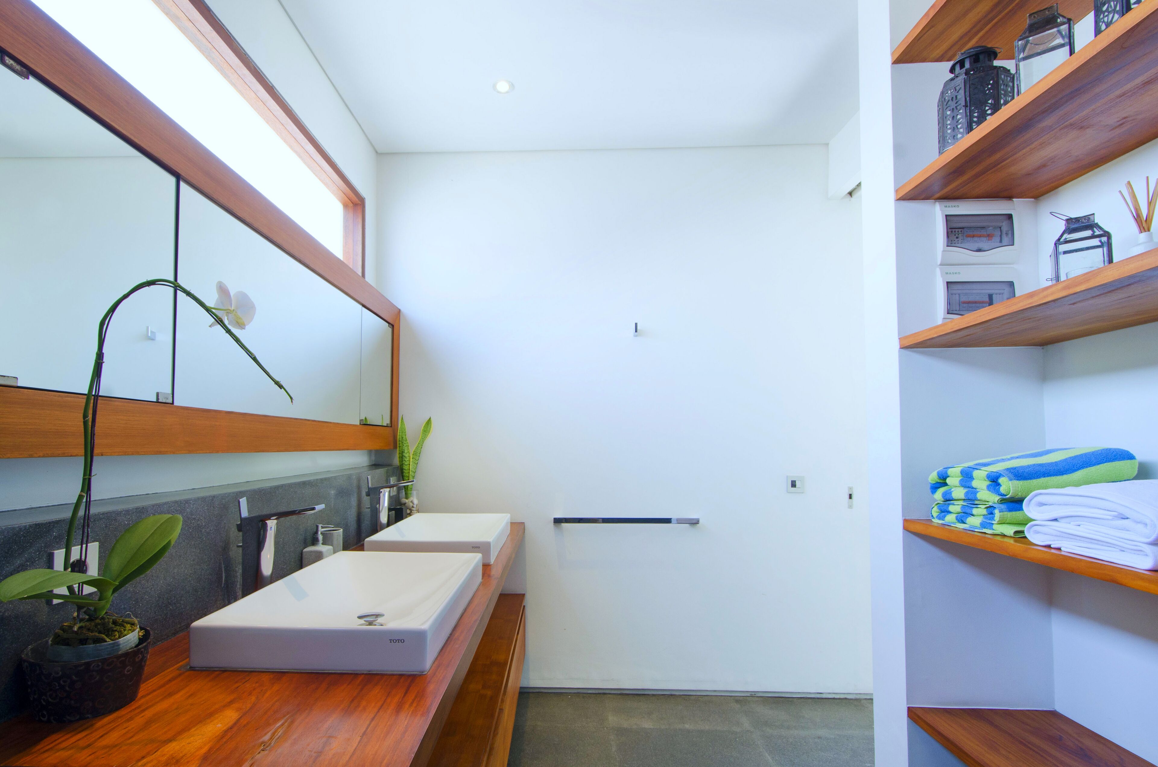 A modern bathroom with a wooden vanity, two sinks, a large mirror, and a shelf with towels.