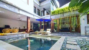 A swimming pool with lounge chairs and an umbrella, surrounded by a stone pathway and greenery.