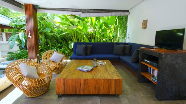 A modern living room with a blue sofa, wicker chairs, a wooden coffee table, and a TV stand with books.