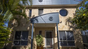 Un edificio con un diseño arquitectónico moderno, que presenta una estructura metálica curva sobre la entrada, una planta en maceta y una pequeña puerta con reja.