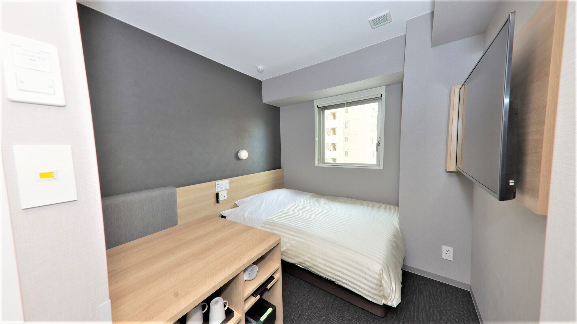 Habitación de hotel pequeña con una cama individual, un escritorio, una silla, una mesita y televisión, además de una ventana.
