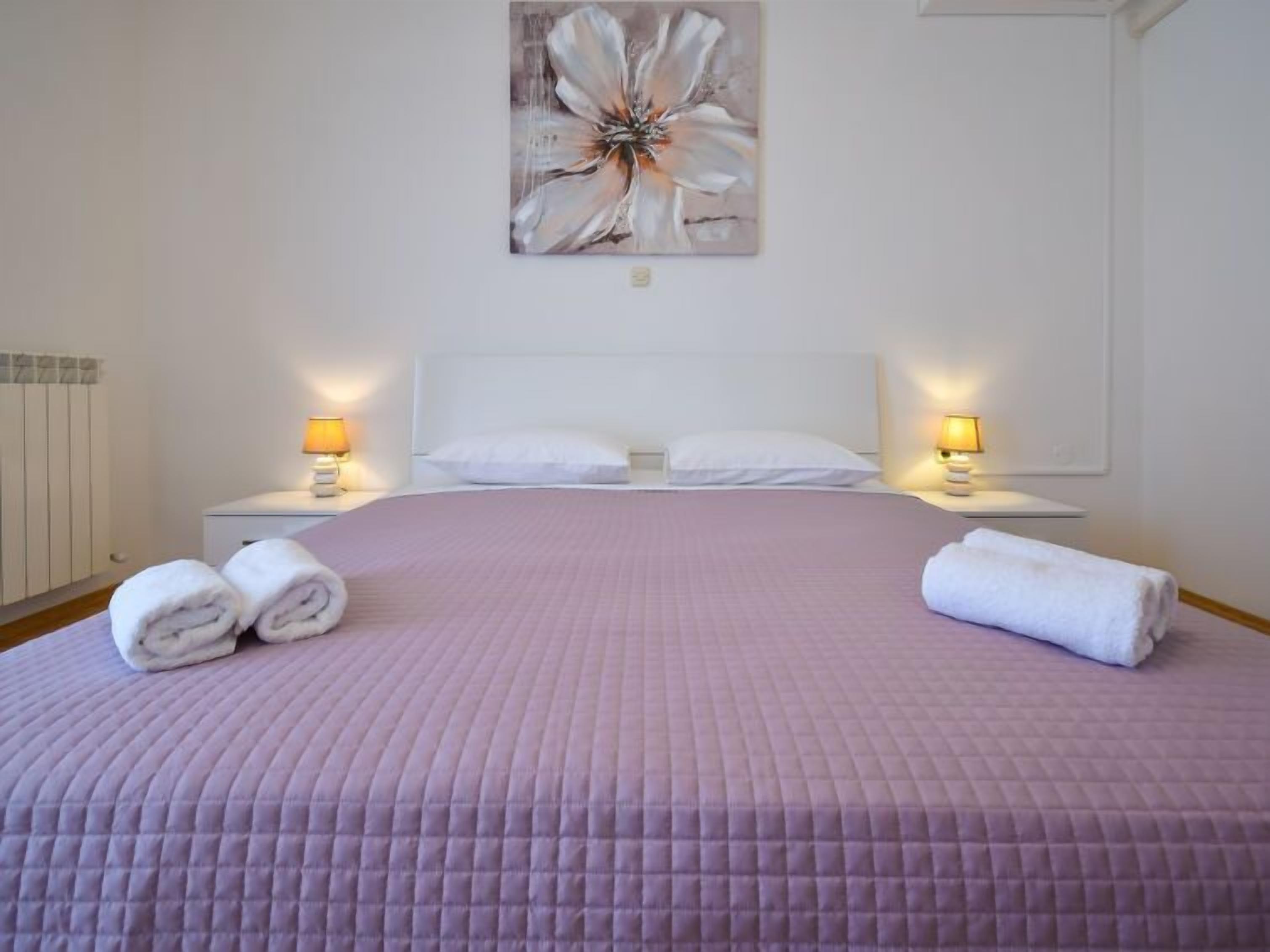 A hotel room with a large bed, two bedside tables with lamps, and a painting on the wall.