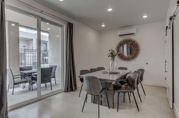 Un comedor moderno con separador de vidrio, un espejo redondo y una mesa de comedor con sillas.
