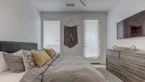 Une chambre à coucher comprenant un lit, une commode, un téléviseur fixé au mur et une porte avec des stores.