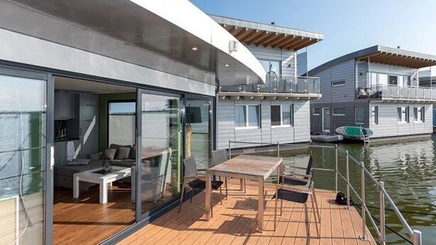 A modern boat with a wooden deck, glass walls, and a dining area.
