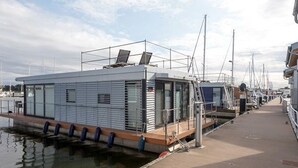 A floating houseboat docked at a marina with a covered deck and windows.