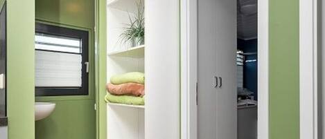 A compact kitchen with a window, a white sink, and a white cabinet with shelves.