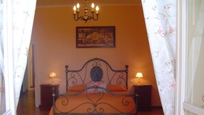 A bedroom with a metal bed frame, two bedside lamps, a chandelier, a red rug, and a painting on the wall. - Central Apartment with terrace over gardens (Orvieto)