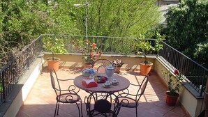 A round table with four chairs on a tiled patio, surrounded by potted plants and a railing. - Central Apartment with terrace over gardens (Orvieto)
