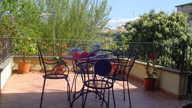 A terrace with a table and chairs, surrounded by potted plants and a railing. - Central Apartment with terrace over gardens (Orvieto)