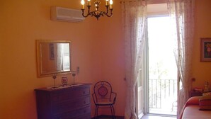 A bedroom with a dresser, a chair, a bed, a chandelier, and a window with curtains. - Central Apartment with terrace over gardens (Orvieto)