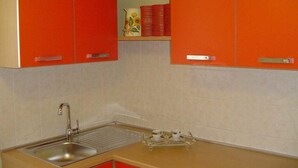 A kitchen with red cabinets, a stainless steel sink, and a small shelf with books and a vase. - Central Apartment with terrace over gardens (Orvieto)