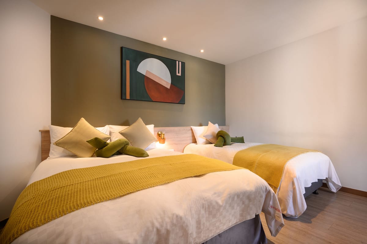 A hotel room with two beds, a large abstract painting on the wall, and a yellow throw blanket on one bed.