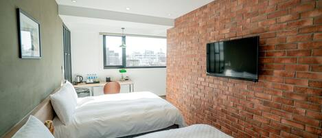 Een hotelkamer met twee bedden, een bureau, een aan een bakstenen muur bevestigde televisie en een raam met uitzicht op de stad.