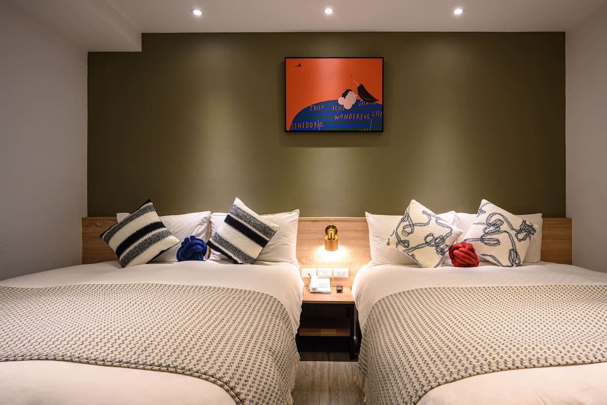 A double room with two beds, a nightstand with a lamp, and a wall-mounted artwork.