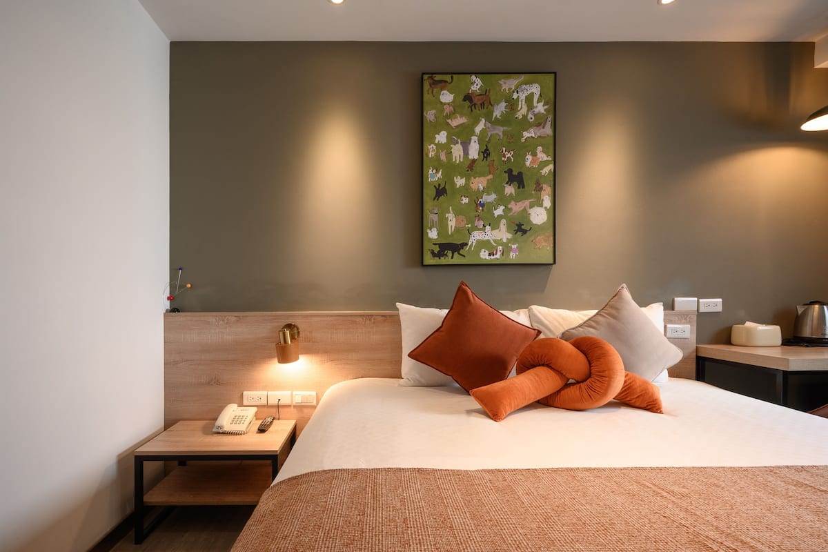 A hotel room with a large bed, a nightstand with a lamp, a telephone, and a painting on the wall.