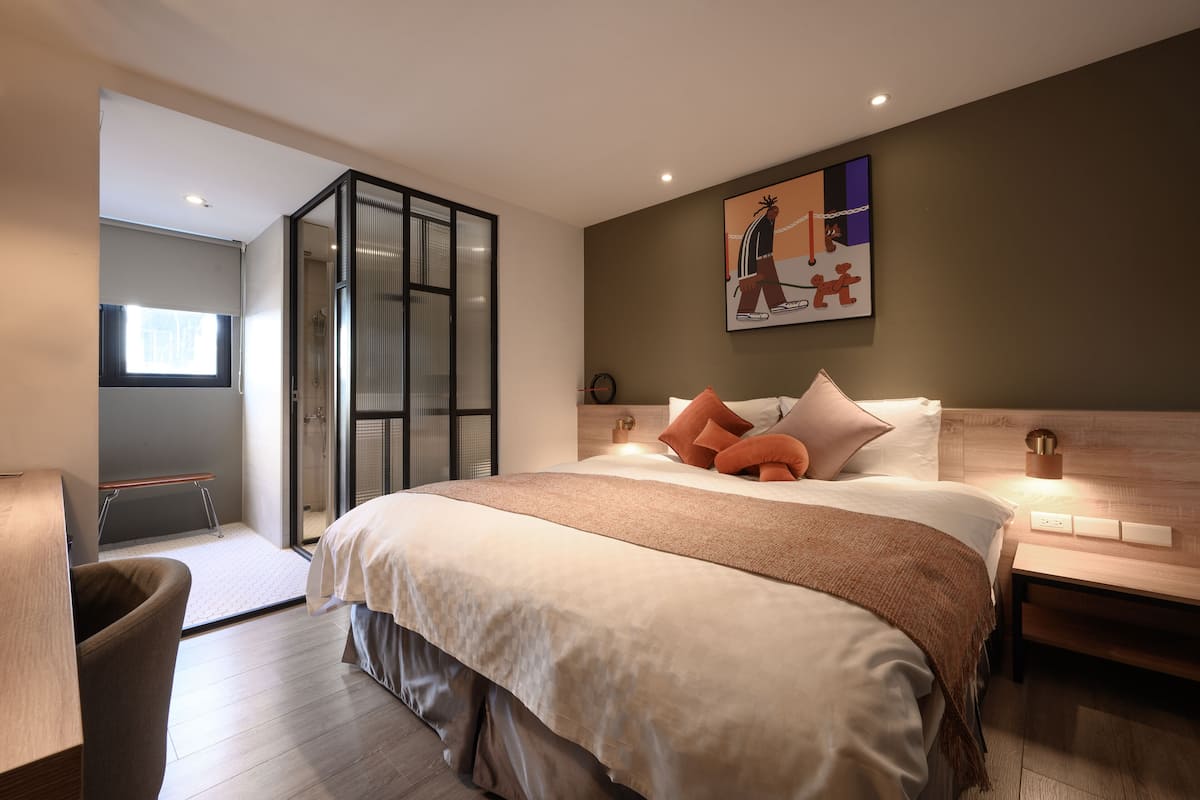 A modern bedroom with a large bed, a bench, and a glass door leading to a shower area.