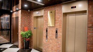 Een moderne lift met een digitaal scherm, een bakstenen muur en een potplant.