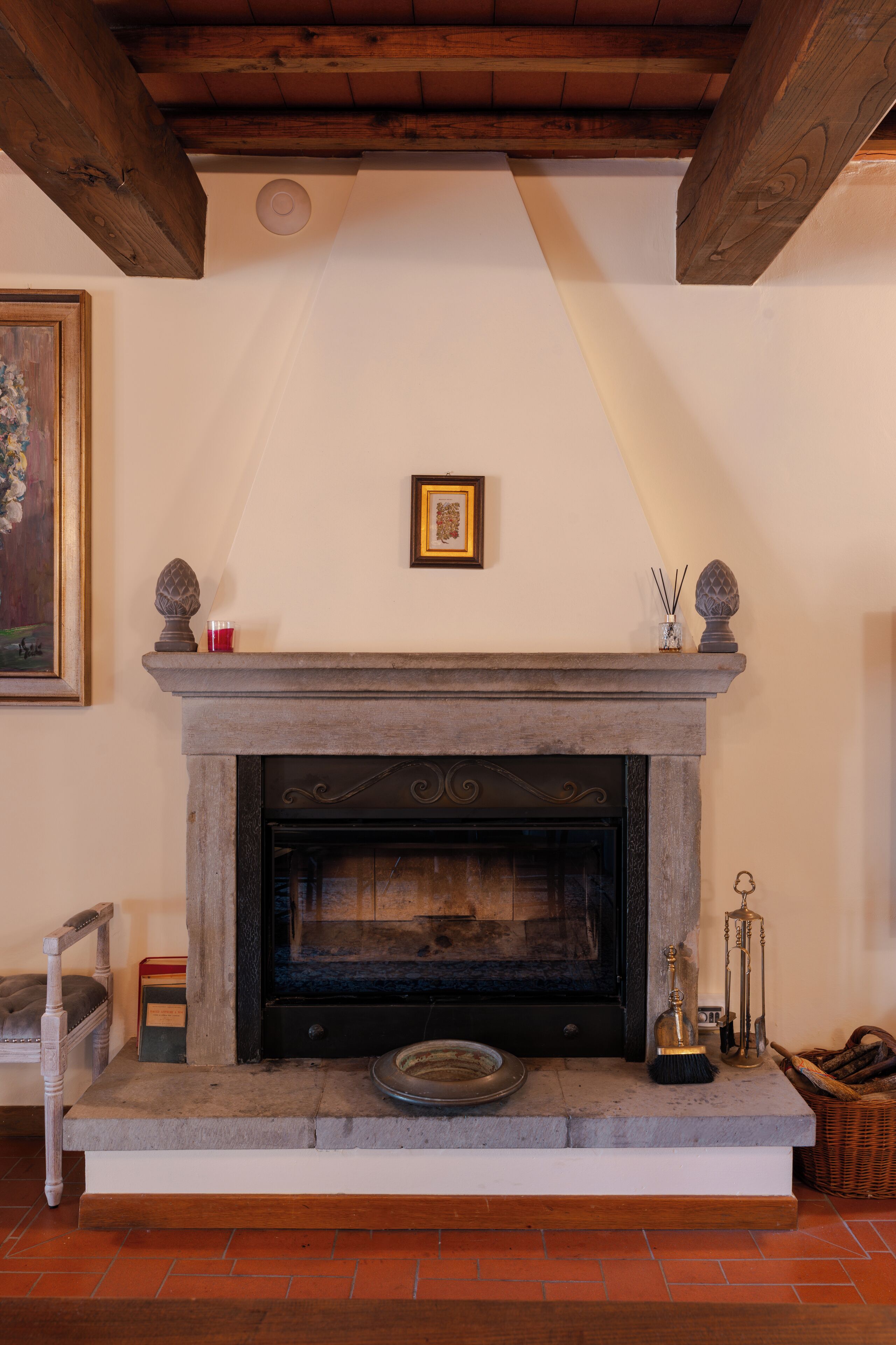 Une cheminée avec un manteau en pierre, un tableau encadré au-dessus, et un plafond avec une poutre en bois.