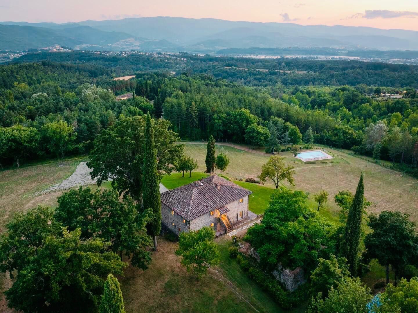 Une maison en pierre, avec un toit de tuiles, entourée d’une végétation luxuriante et dotée d’une piscine.