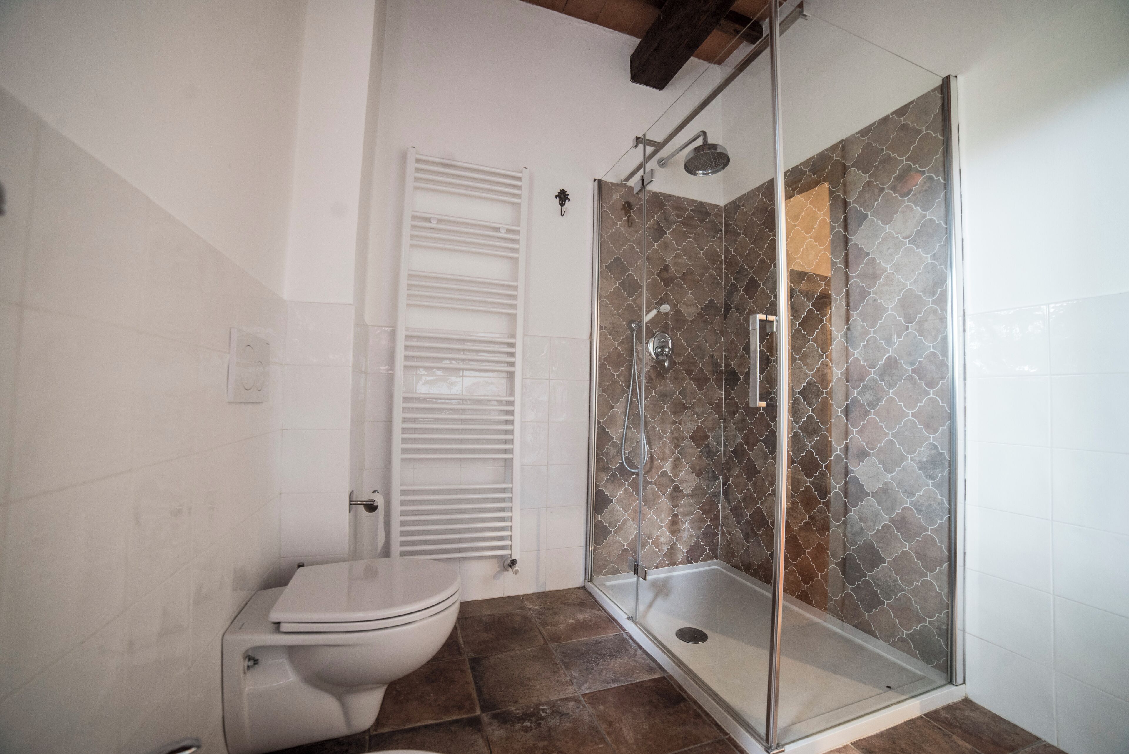 A bathroom with a toilet, a glass-enclosed shower, and tiled walls.