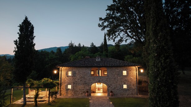 Une maison en pierre avec un toit en tuiles, une arche centrale et une entrée pavée.