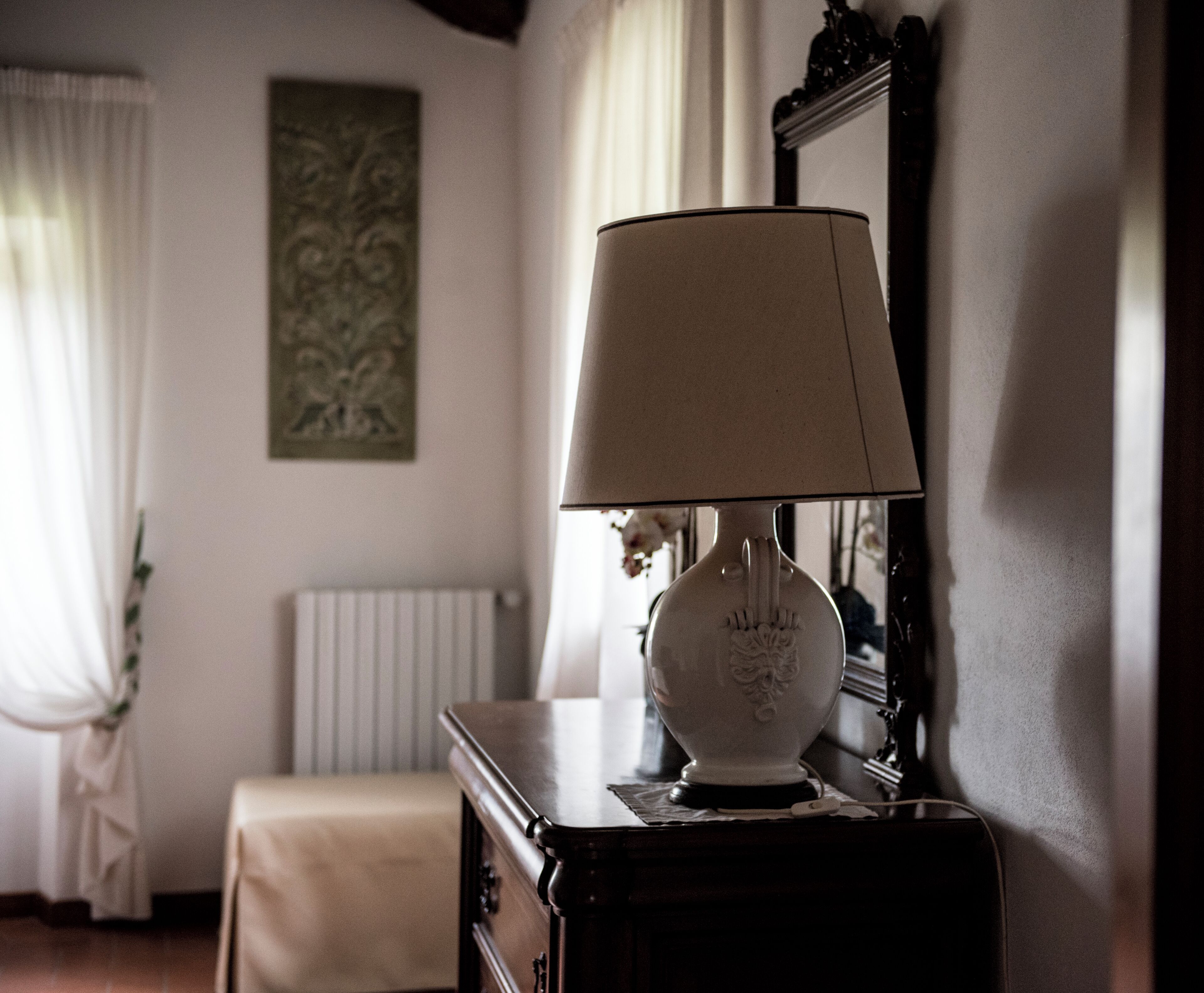 Une pièce avec une lampe sur une commode, un radiateur et un tableau accroché au mur.