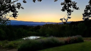 Un paysage avec une piscine entourée de verdure et d’arbres, offrant une vue sur des collines lointaines.