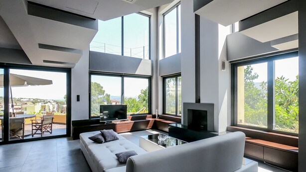 A modern living room with a sofa, TV, and fireplace, large windows offering a view of the outdoors. - Villa Opuntia (Chania)