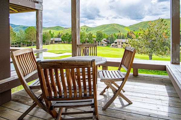 A wooden deck with a table and chairs, overlooking a green landscape with hills and buildings. - Panoramic Views! Designer`s Condo on Golf Course w/Resort Amenities (Sun Valley)