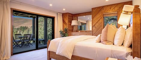 A bedroom with a large bed, a wooden headboard, a nightstand, a mirror, and a view of an outdoor deck with chairs.