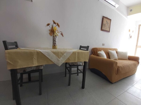 Ein Essbereich mit Tisch und Stühlen, einer Vase mit Trockenblumen und einem braunen Sofa mit Kissen.