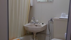 A small bathroom with a toilet, sink, and shower curtain. - Business Hotel Goto (Kure)