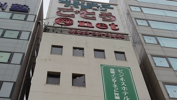 A hotel with a green vertical sign indicating a business center and a red sign with Japanese characters. - Business Hotel Goto (Kure)