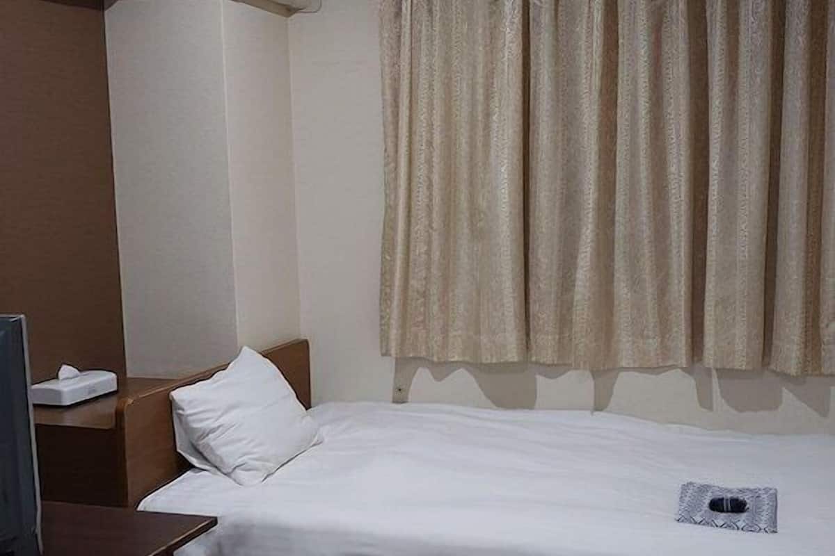 Una camera d'albergo con un letto, un comodino, una televisione e una finestra con tende.