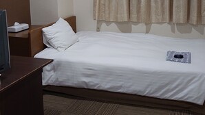 A hotel room with a single bed, a bedside table with a lamp, a wall-mounted air conditioner, and a window with patterned curtains. - Business Hotel Goto (Kure)