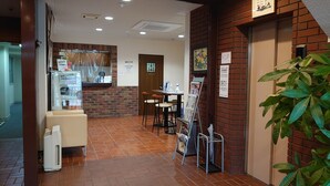 A reception area with a counter, seating, and a plant. - Business Hotel Goto (Kure)
