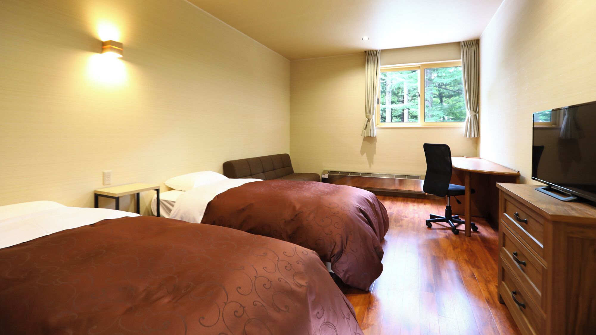 A hotel room with two beds, a desk, a chair, a television, and a window with curtains.
