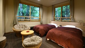 Habitación de hotel con dos camas, una mesita redonda pequeña, dos sillones y ventanas grandes con cortinas.