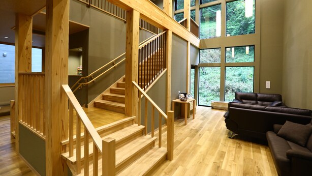 Amplia sala de estar con escalera de madera, ventanas grandes y sofá de cuero.